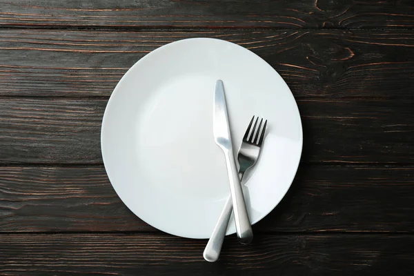 Tahta arka planda çatal ve bıçaklı tabak, üst manzara.