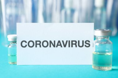 Inscription Coronavirus and bottle of vaccine on blue background