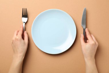Female hands hold fork and knife on craft background with plate,