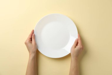 Female hands hold plate on beige background, top view