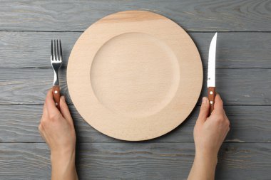 Female hands hold fork and knife on wooden background with plate