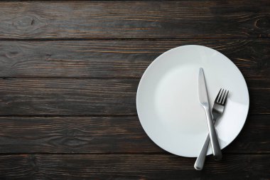 Tahta arka planda çatal ve bıçaklı tabak, üst manzara.