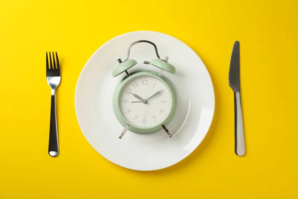 Bord met wekker, vork en mes op gele achtergrond, bovenkant — Stockfoto
