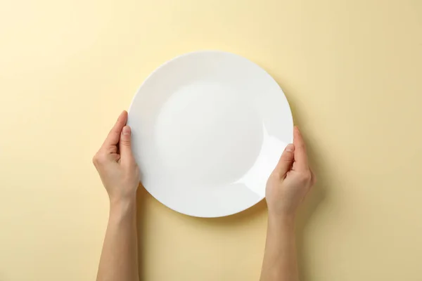 Female hands hold plate on beige background, top view — Stok fotoğraf