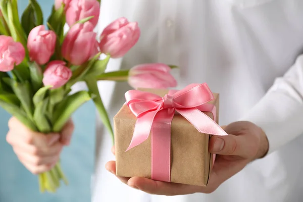 Hombre sostiene ramo de tulipanes rosados y regalo sobre fondo azul, cl —  Fotos de Stock