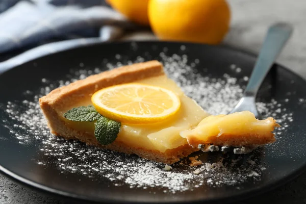 Plate with lemon tart slice on grey background with towel and le