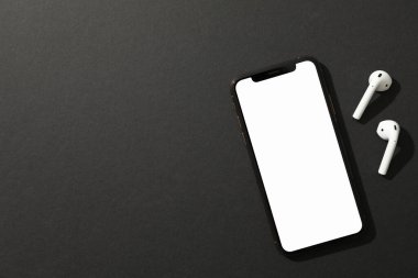 Boş ekranlı telefon ve siyah arka planda kulaklık, üst 
