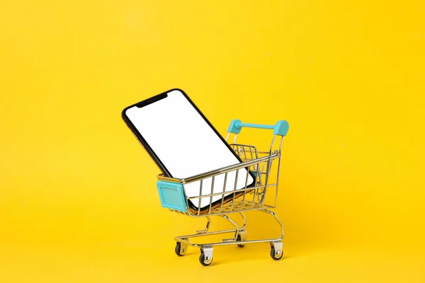 Phone with empty screen and shopping cart on yellow background, — Stock Photo, Image