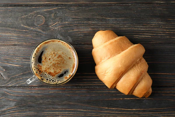 Croissant e xícara de café em fundo de madeira, vista superior — Fotografia de Stock