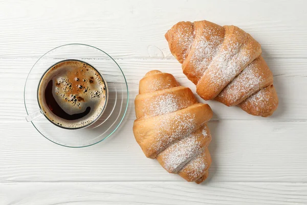 Kopp med kaffe och croissanter på trä bakgrund, ovanifrån — Stockfoto