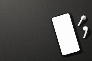Boş ekranlı telefon ve siyah arka planda kulaklık, üst 