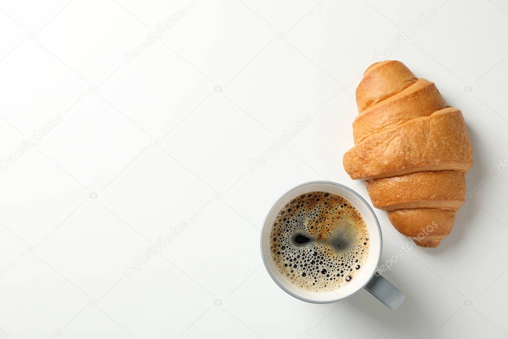Croissant and cup of coffee on white background, top view