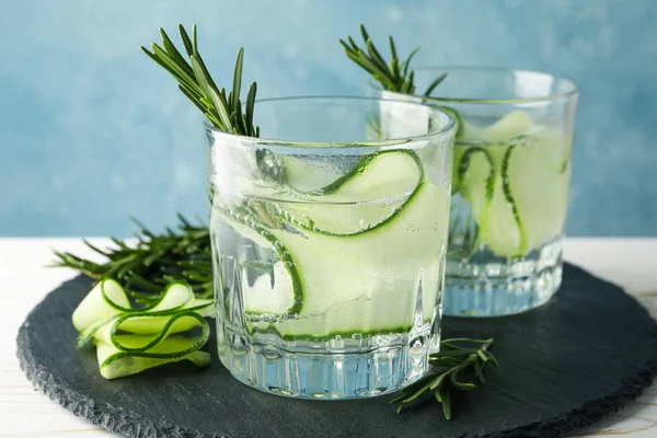 Glasses with cucumber water on tray on wooden table, close up