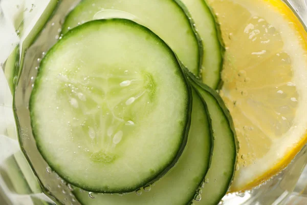 Glass with cucumber water and slices, and lemon, close up