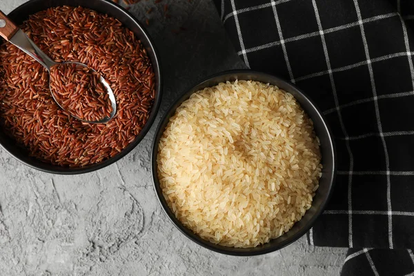 Bowls with rice, spoon and towel on grey background, top view