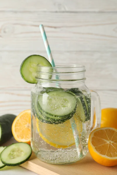 Glass jar of cucumber water, slices and lemons on wooden background, close up