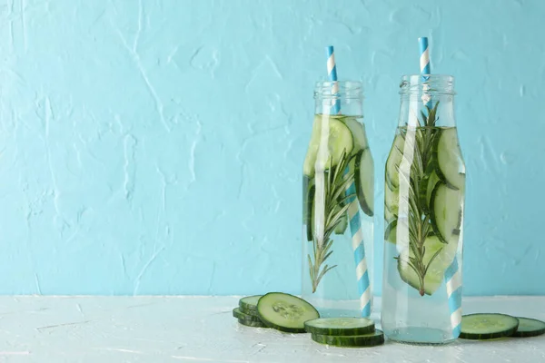 Composition with bottles of cucumber water against blue background, space for text