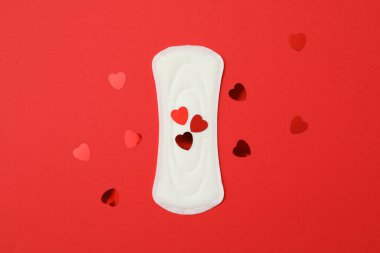 Kırmızı arka planda hijyenik ped ve küçük kalpler.