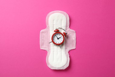 Pembe arka planda alarm saati olan hijyenik ped.
