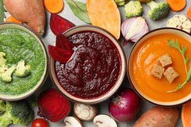 Gri arka planda sebze çorbaları ve malzemeler, üst görünüm