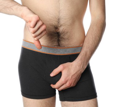 Kasığını tutan ve baş parmağını aşağı gösteren beyaz arka planda izole edilmiş bir adam.