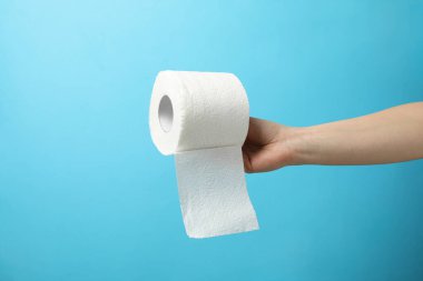 El ele tutuşan tuvalet kağıdı rulosu mavi arka planda