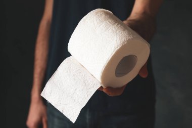 Tişörtlü adam tuvalet kağıdı tutuyor.