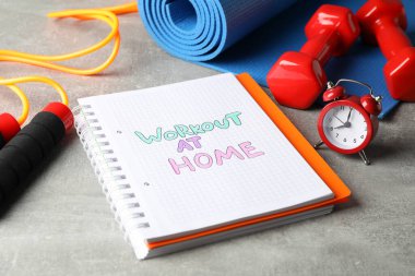 Evde antreman ve gri arka planda fitness malzemelerinin olduğu kitapçık