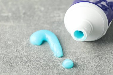 Gri arkaplanda diş macunu ve tüpten yapılmış soru işareti, yakın plan