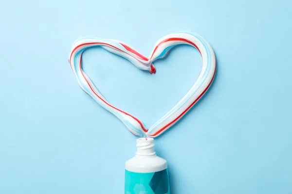 Heart made of toothpaste and tube on blue background, top view