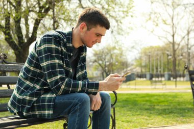 Adam parkta bankta otururken akıllı telefon kullanıyor.