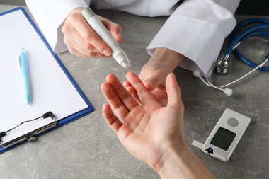 Gri masadaki hasta diyabetindeki kan şekerini ölçen doktor.