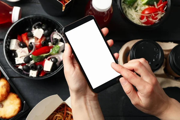 Woman holds smartphone. Food in takeaway boxes on wooden background