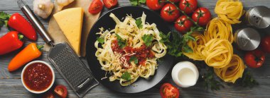 Lezzetli makarna ve ahşap arka planda yemek pişirmek için malzemeler içeren kompozisyon