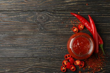 Ahşap arka planda kırmızı biber ve cam sos kavanozu.