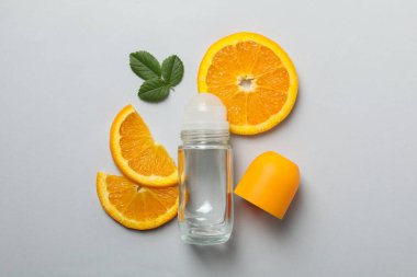 Vücut deodorantları yuvarlanıyor, yapraklar ve turunçgiller gri arka planda