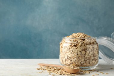 Beyaz ahşap masada yulaf ezmeli ve kaşıklı cam kavanoz.