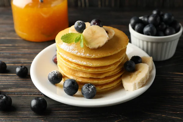 Composition with pancakes, banana, blueberry and jam on wooden background