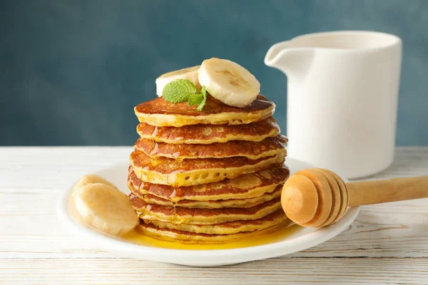 Pancakes with banana and honey on white wooden table