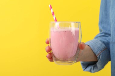 Kadın sarı arka planda bir bardak çilekli milkshake tutuyor.