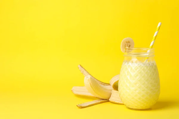 Glass of banana milkshake on yellow background. Summer drink