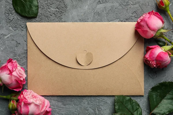 Craft paper envelope and roses on gray background, close up