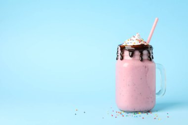 Mavi arka planda bir kavanoz lezzetli çilekli milkshake.