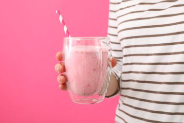 Kadın pembe arka planda bir bardak çilekli milkshake tutuyor.