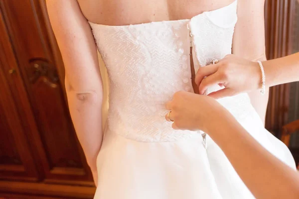 Dama de honor está ayudando a la novia a abotonar el vestido de novia —  Fotos de Stock
