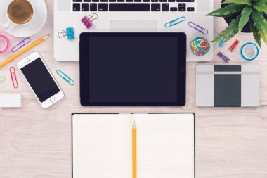 Macbook dizüstü bilgisayar, ipad dijital tablet, iphone akıllı telefon ve kalemli açık not defteri ile ofis masası işyeri üst görünümü
