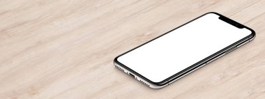 Iphone X maketine benzer izometrik siyah akıllı telefon, fotokopi alanı olan ahşap ofis masası afişinin üzerinde yatıyor