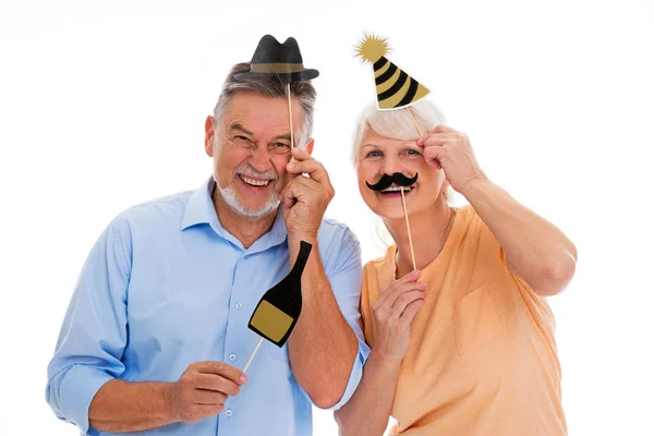 Funny senior couple holding party hats and mustaches on sticks — Stock Photo, Image