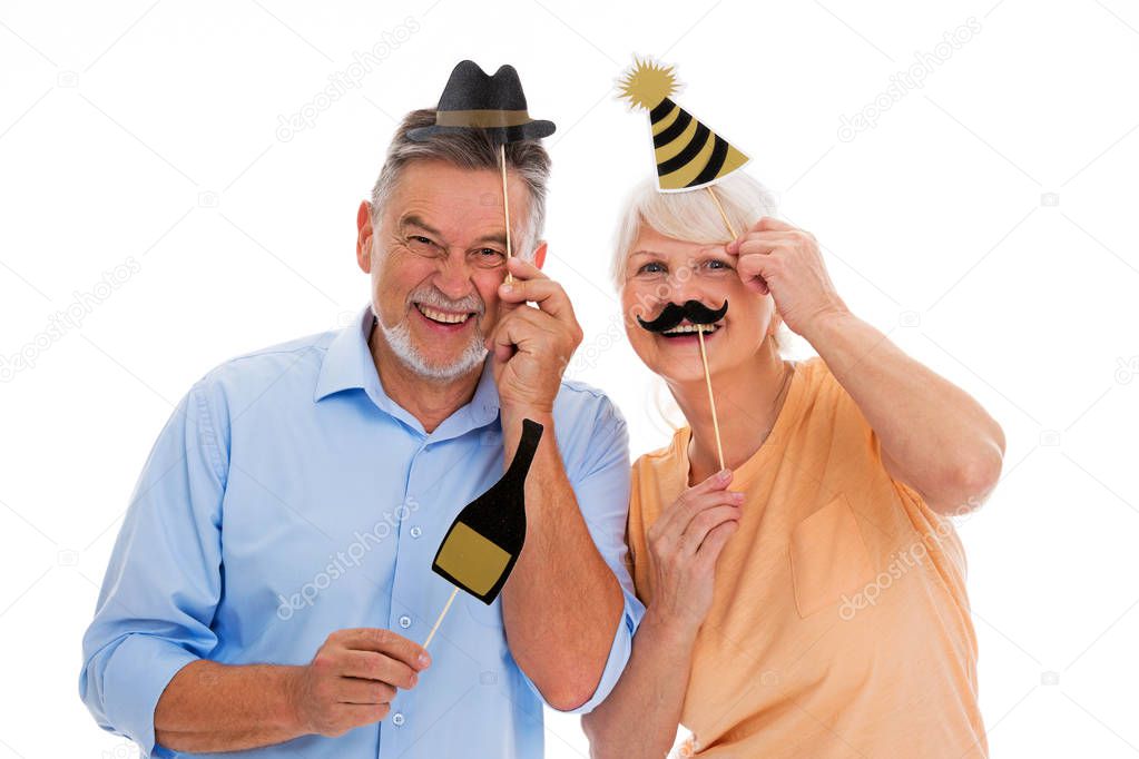 Funny senior couple holding party hats and mustaches on sticks