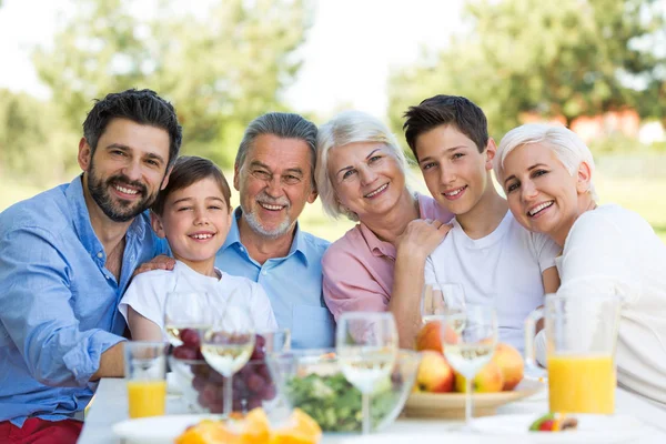 Family sitting at table outdoors, smiling — Stock Photo, Image